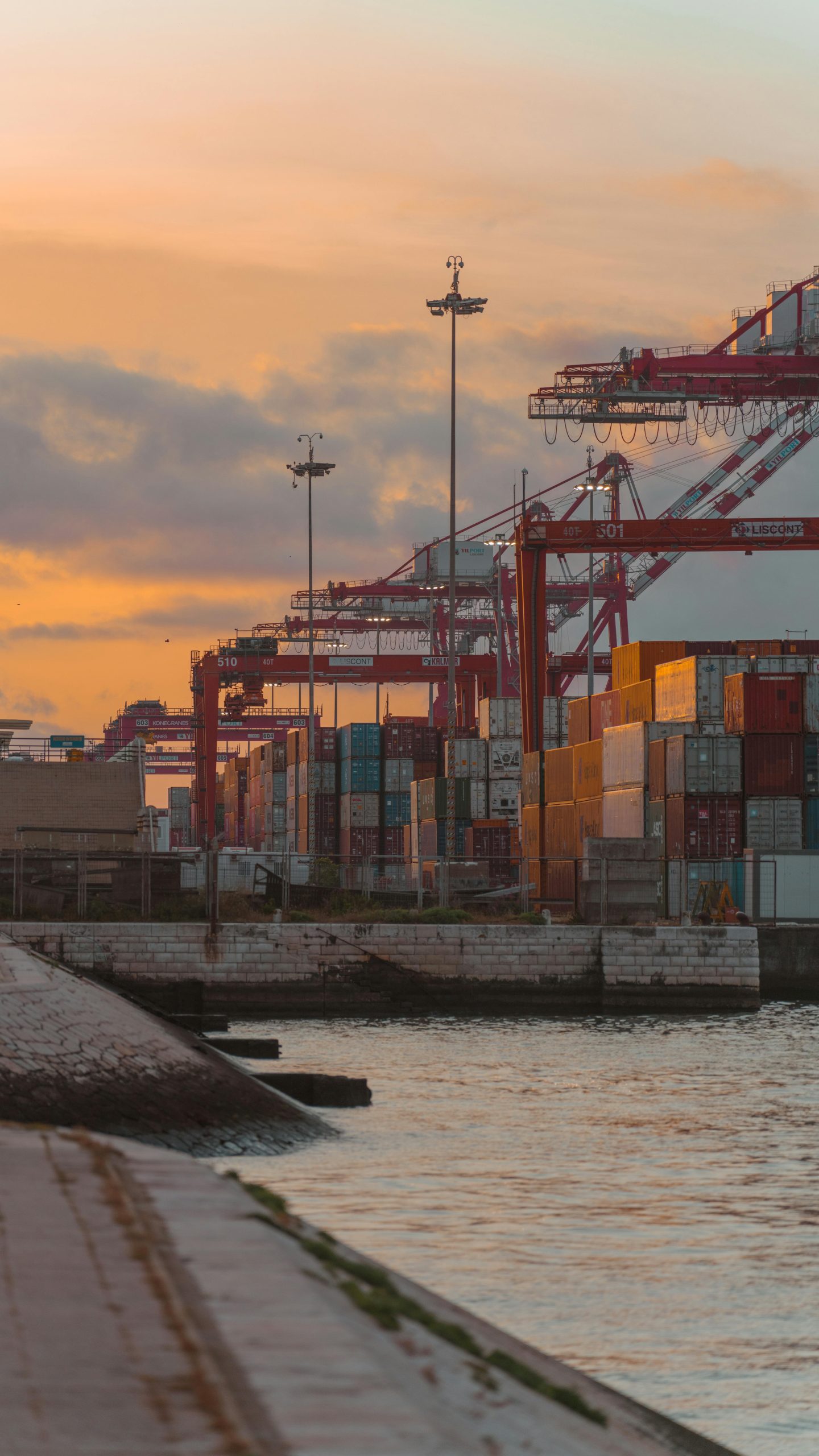 Colorful shipping containers and cranes at a port during sunset.